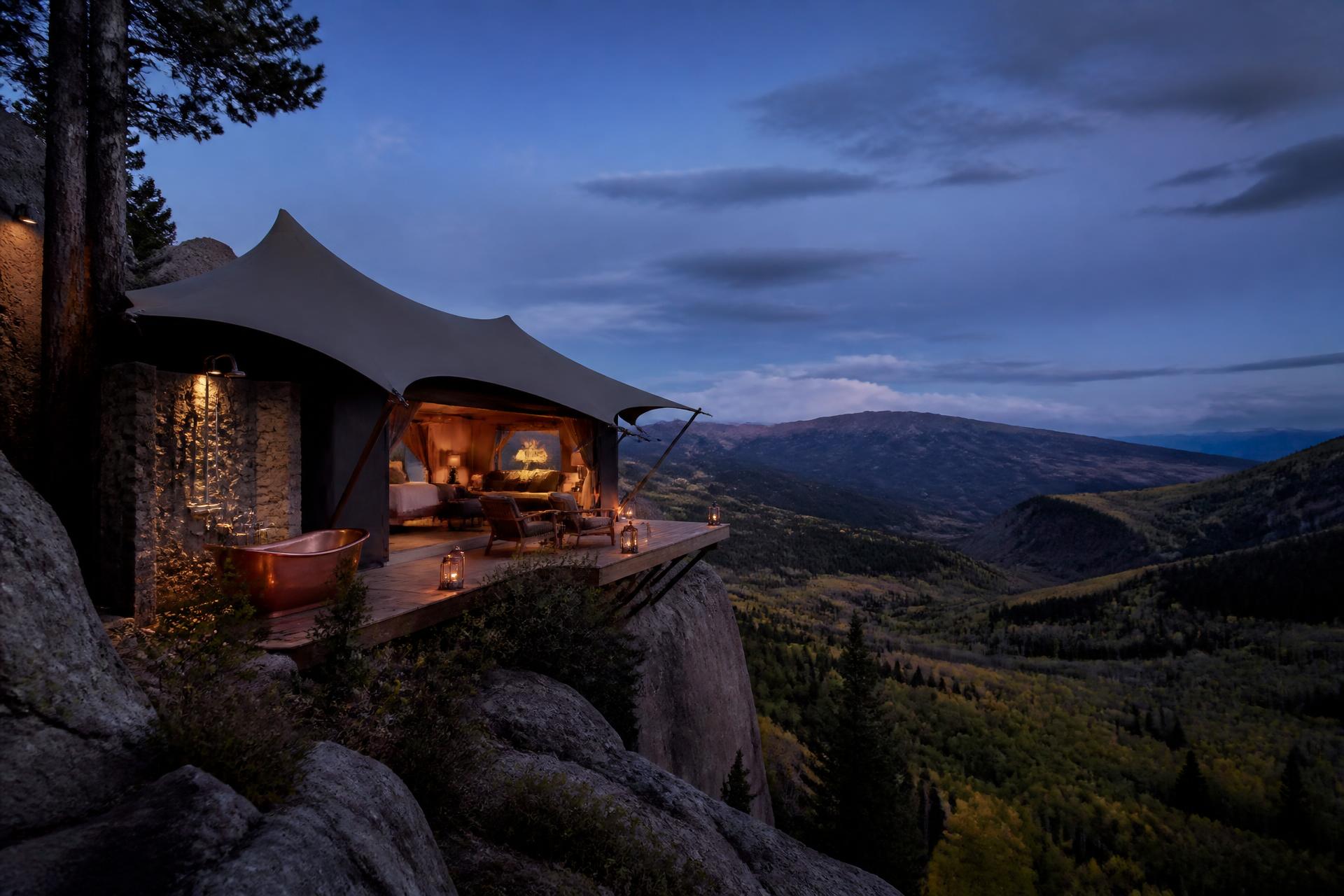 A cantilevered deck reaches over the canyon lip — copper soaking tub, stone shower and lantern light held against the blue hour.